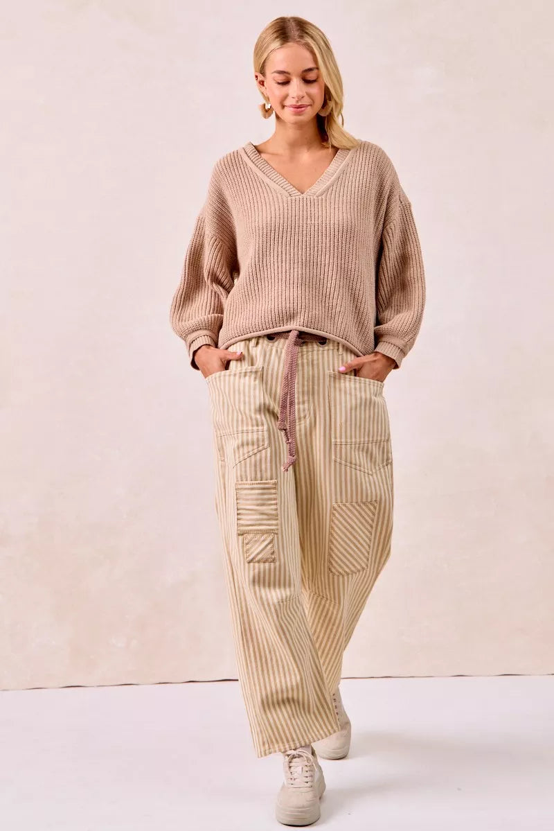 Woman wearing a beige sweater and pants against a plain background