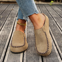 Brown suede loafers worn with denim jeans on a wooden floor.
