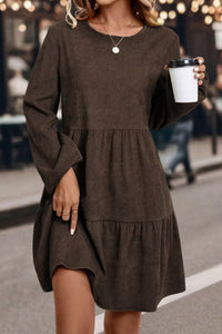Woman wearing a brown dress holding a coffee cup on a street.