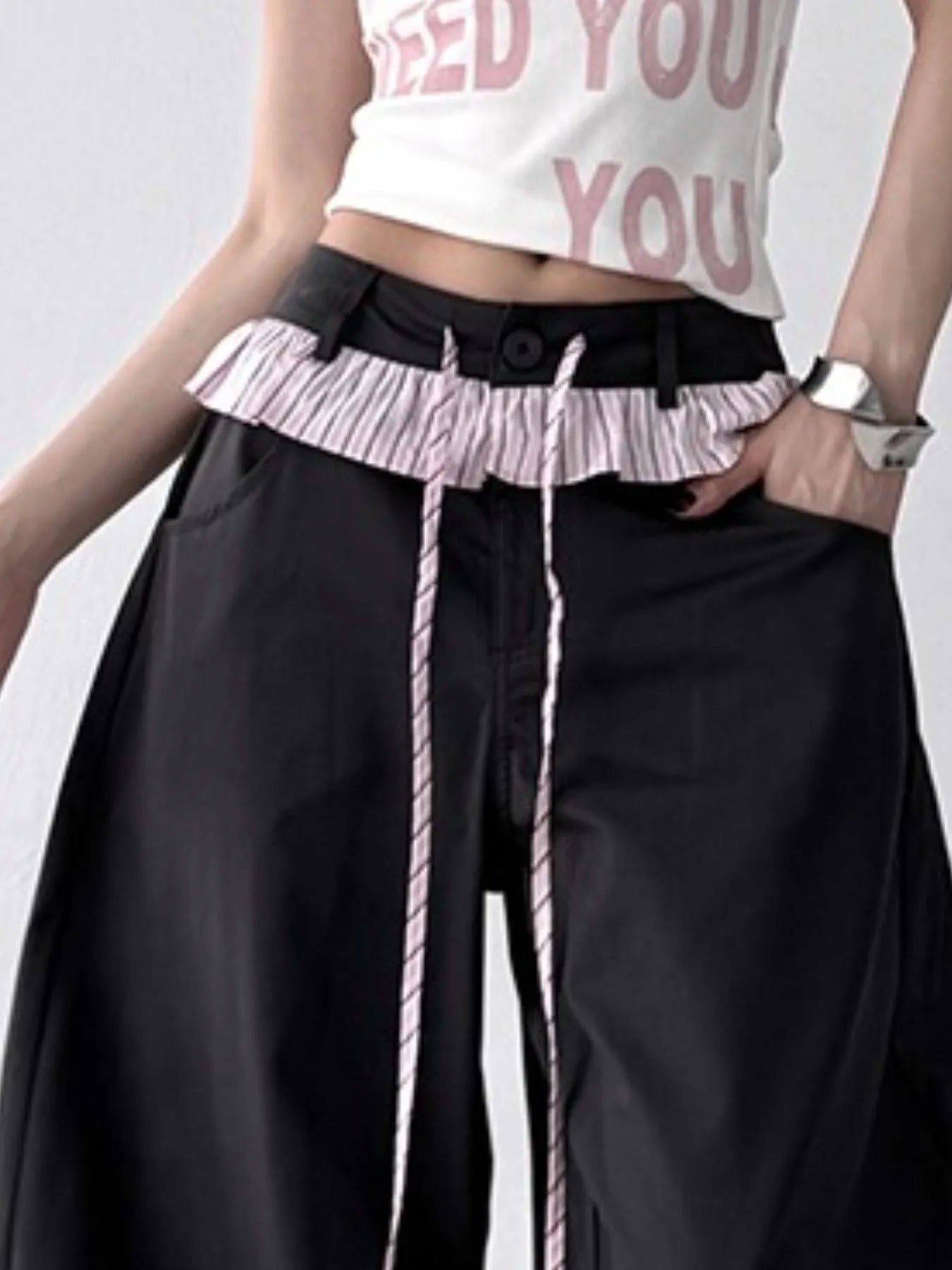Person wearing a white crop top with pink text and black wide-leg pants with a ruffled waistband.