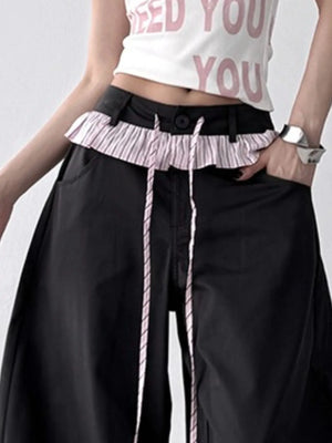 Person wearing a white crop top with pink text and black wide-leg pants with a ruffled waistband.