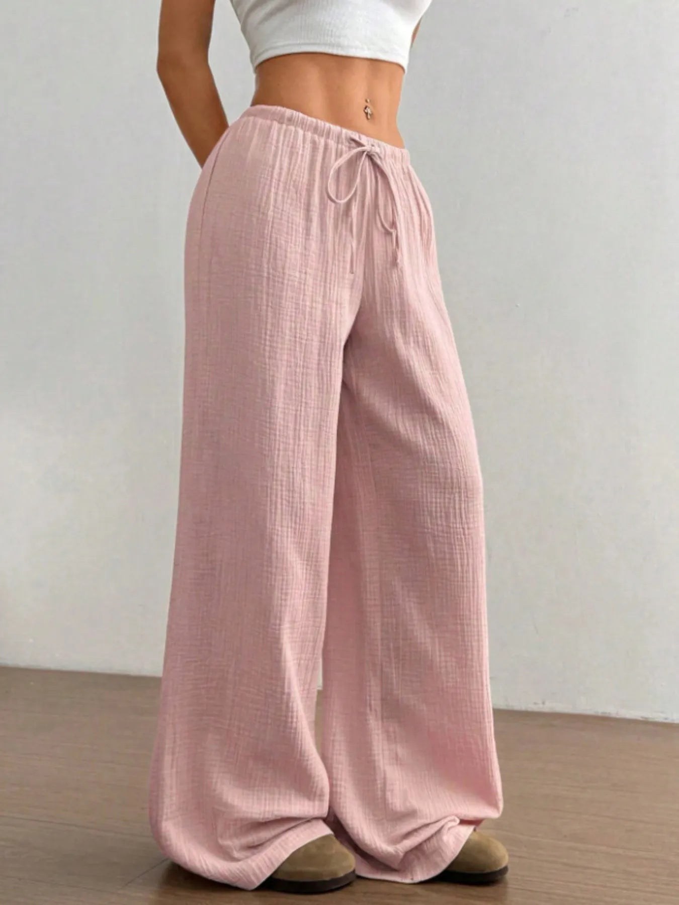 Person wearing pink wide-leg pants and a white top against a plain background