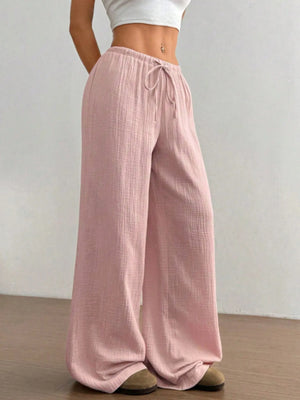 Person wearing pink wide-leg pants and a white top against a plain background
