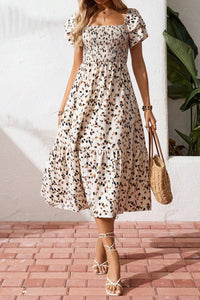 Woman wearing a floral dress holding a straw bag on a brick floor.