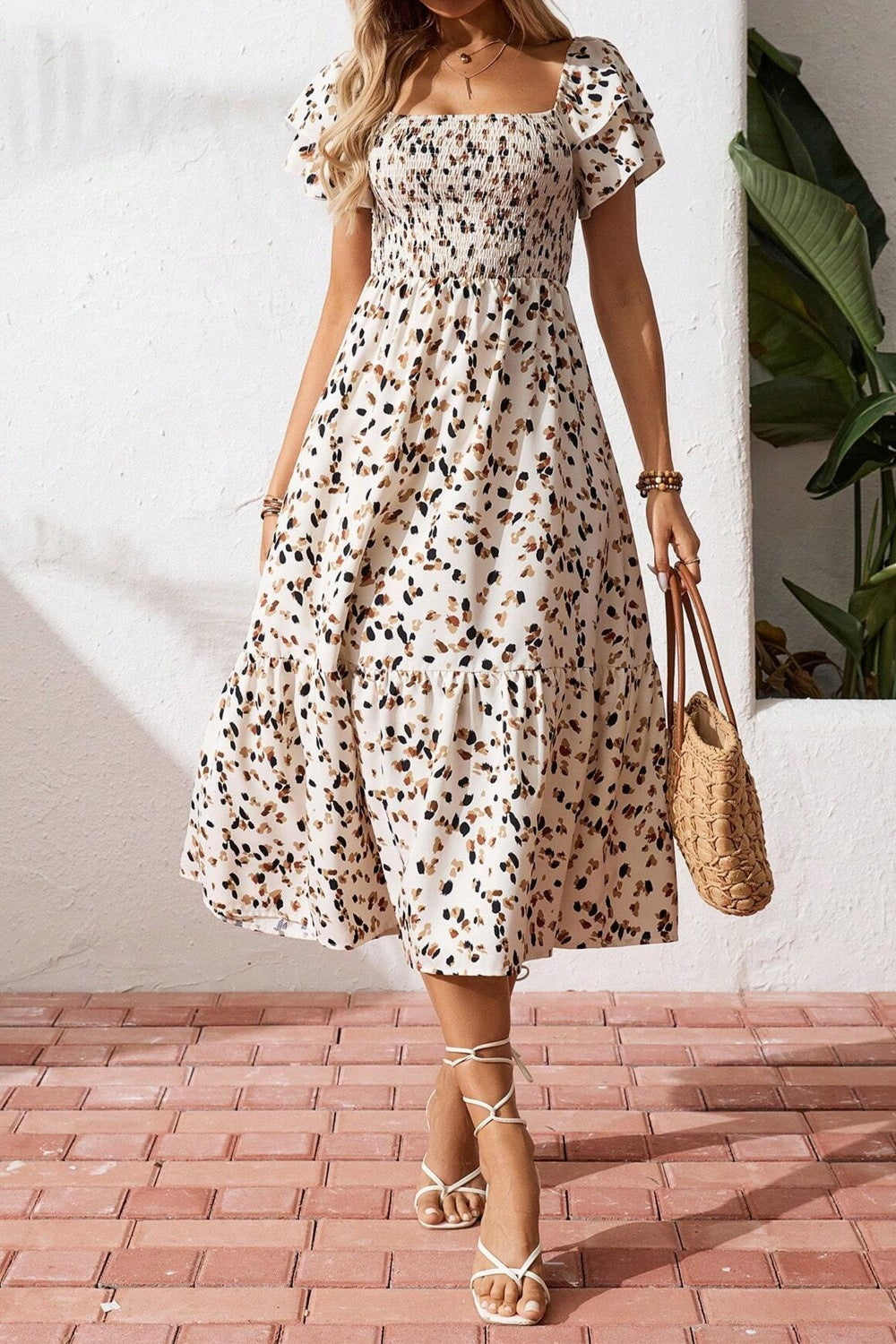 Woman wearing a floral dress holding a straw bag on a brick floor.