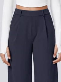 Navy blue pants worn with a white long-sleeve top on a light gray background