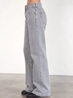 Light gray wide-leg denim jeans shown on a model from the side, paired with black shoes against a plain studio background.