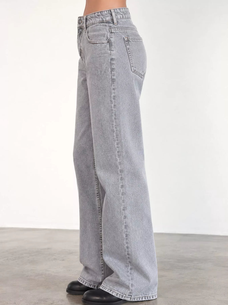Light gray wide-leg denim jeans shown on a model from the side, paired with black shoes against a plain studio background.