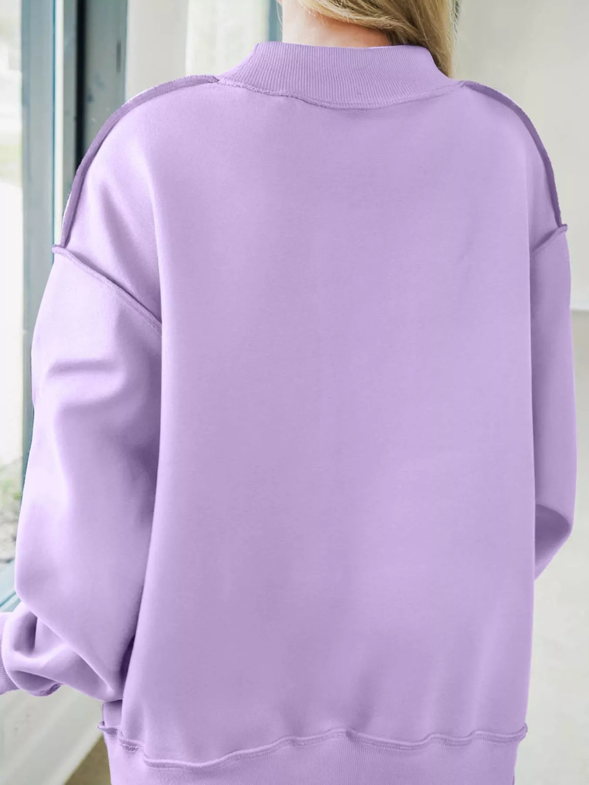 A person viewed from the back wearing an oversized light purple sweatshirt with ribbed collar, cuffs, and hem.