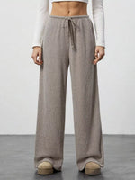 Person wearing beige wide-leg pants with a white top on a plain background