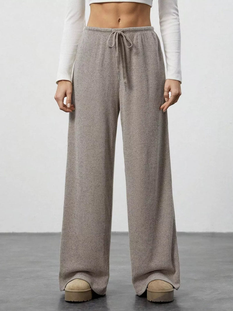 Person wearing beige wide-leg pants with a white top on a plain background