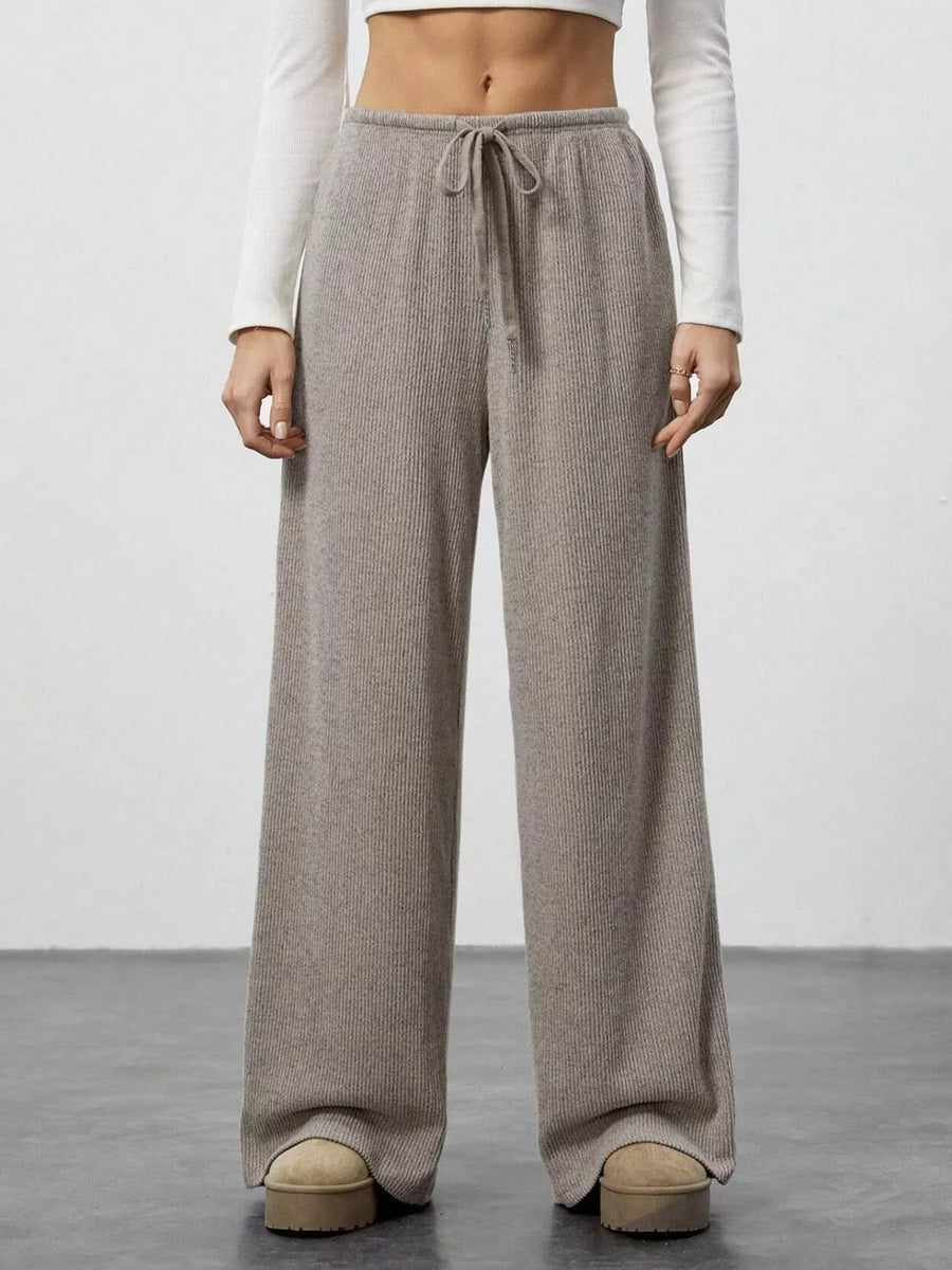 Person wearing beige wide-leg pants with a white top on a plain background