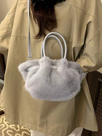 Person holding a fluffy gray handbag with a beige jacket.