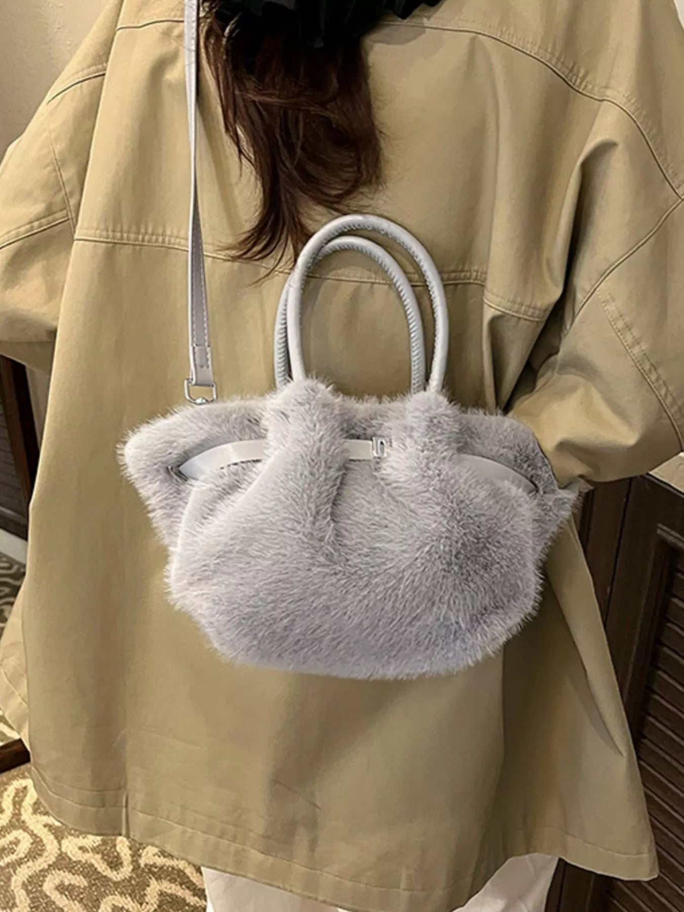 Person holding a fluffy gray handbag with a beige jacket.