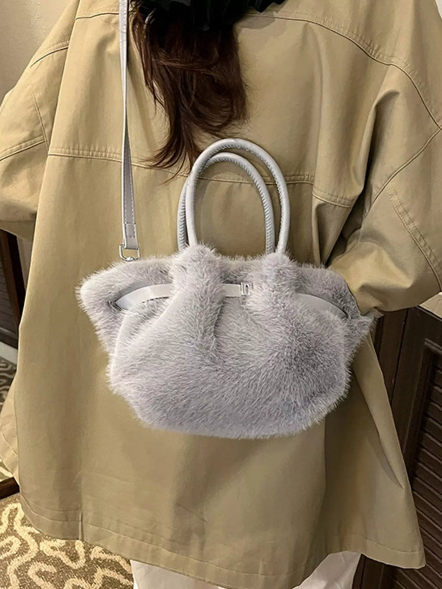Person holding a fluffy gray handbag with a beige jacket.