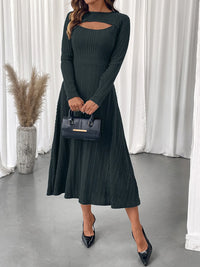 Woman wearing a dark green ribbed dress with cut-out design, holding a black handbag indoors.
