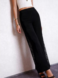 Person wearing black pants with lace detailing against a plain background