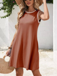 Woman wearing a brown dress with a white wall and greenery in the background