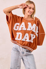 Person wearing a 'GAME DAY' oversized sweatshirt with light blue jeans on a plain background