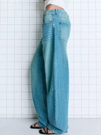 Person wearing light blue jeans against a white tiled wall.