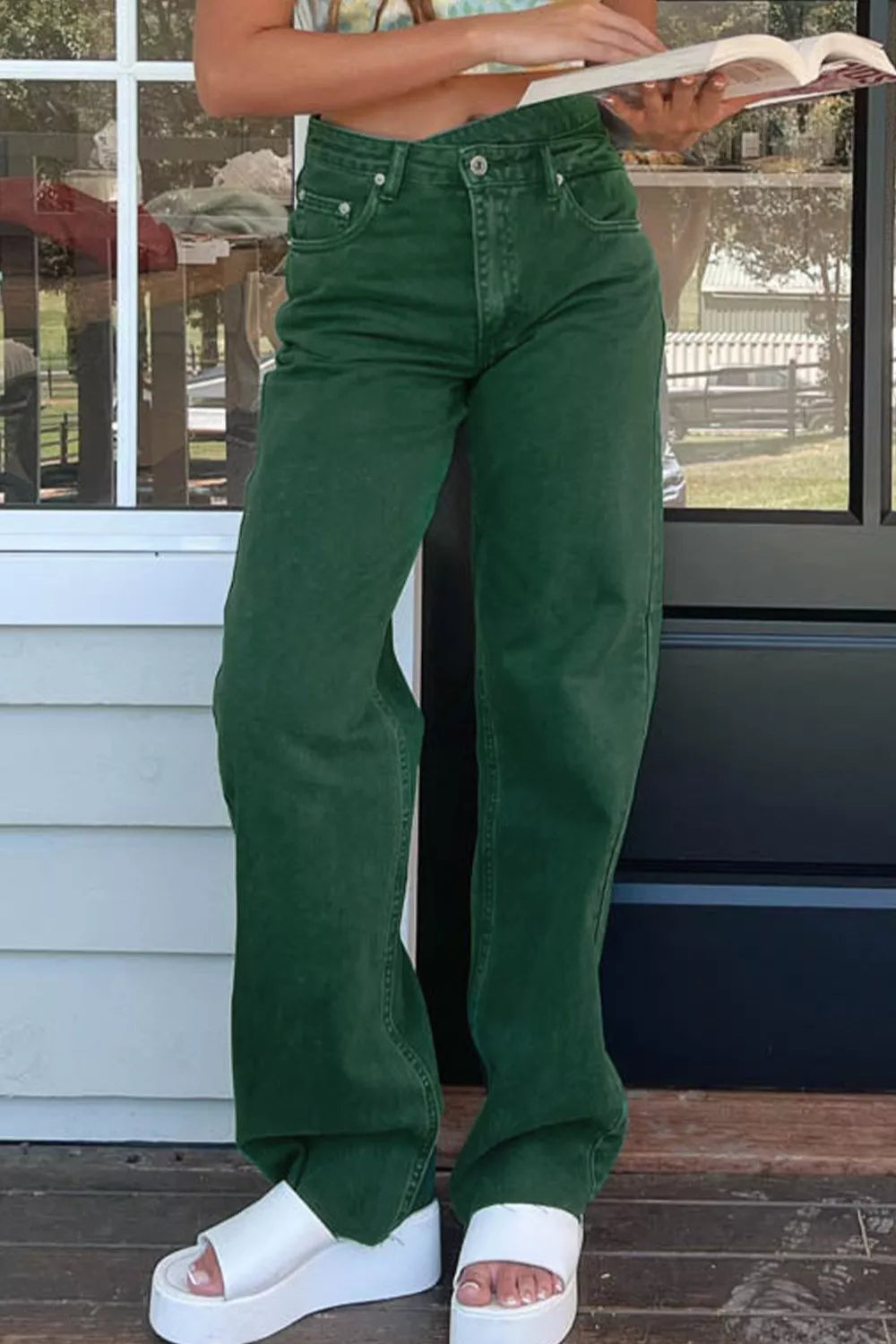 Person wearing green pants and white sandals standing on a wooden deck.