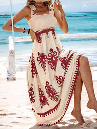 Woman in a white dress with red patterns sitting on a beach.