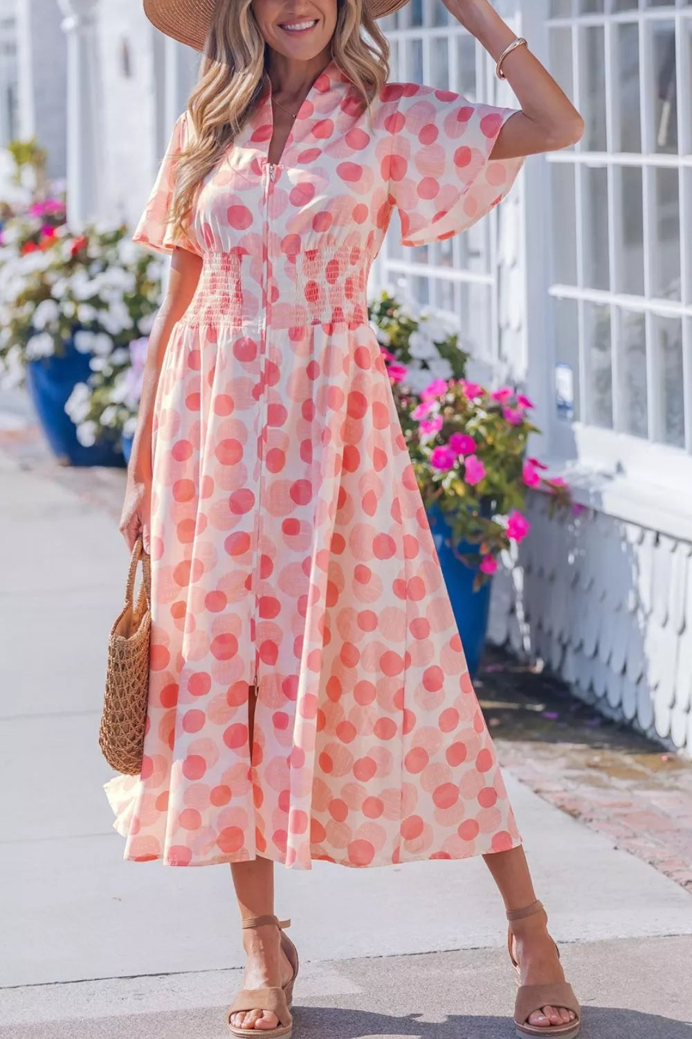Woman wearing a pink polka dot dress standing outdoors with flowers in the background