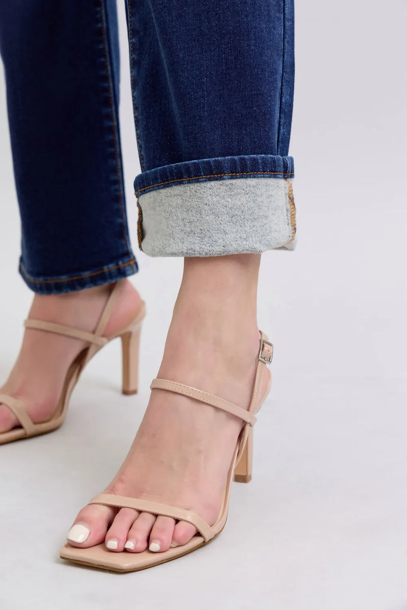 Beige high-heeled sandals worn with rolled-up jeans on a light gray background