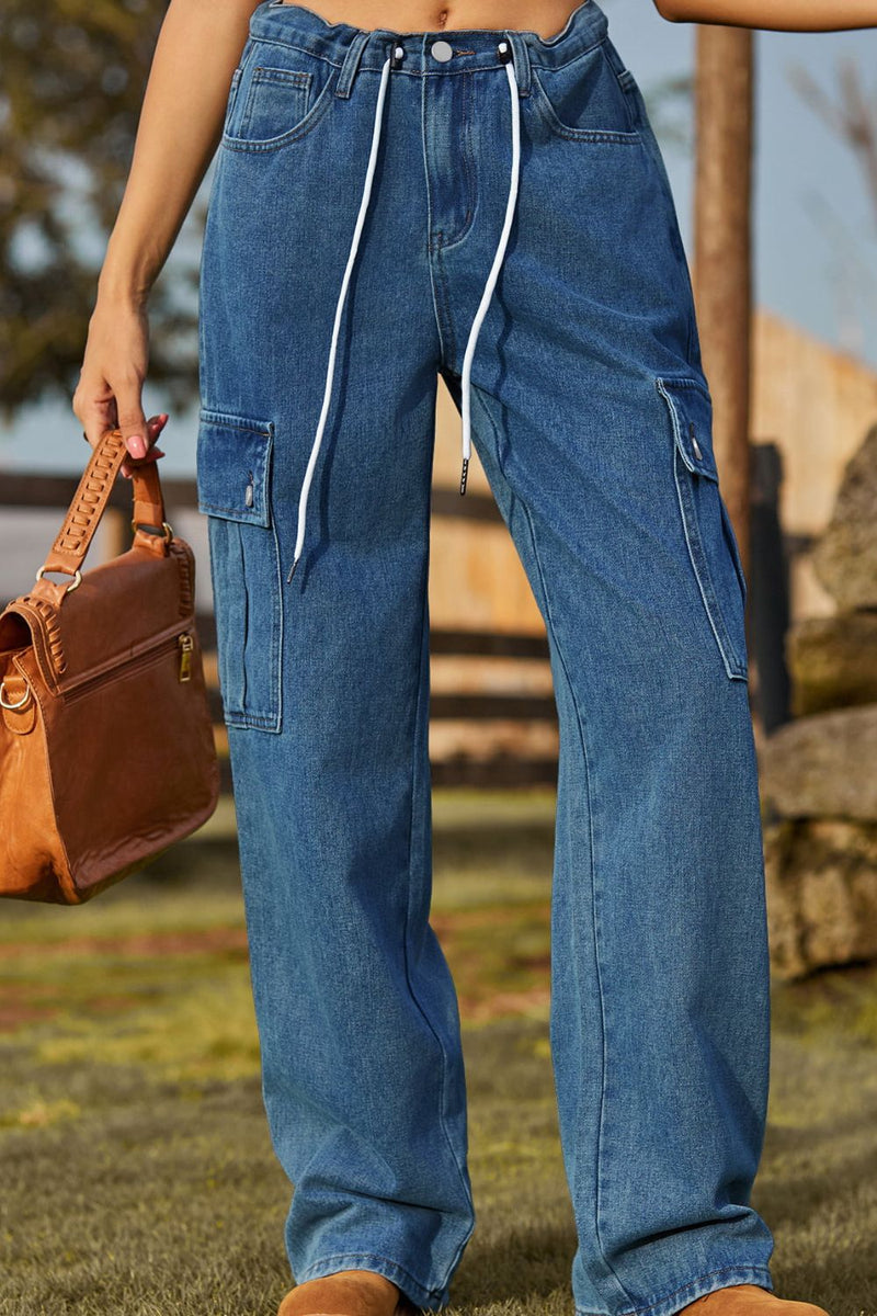 Person wearing blue cargo pants holding a brown leather bag outdoors.
