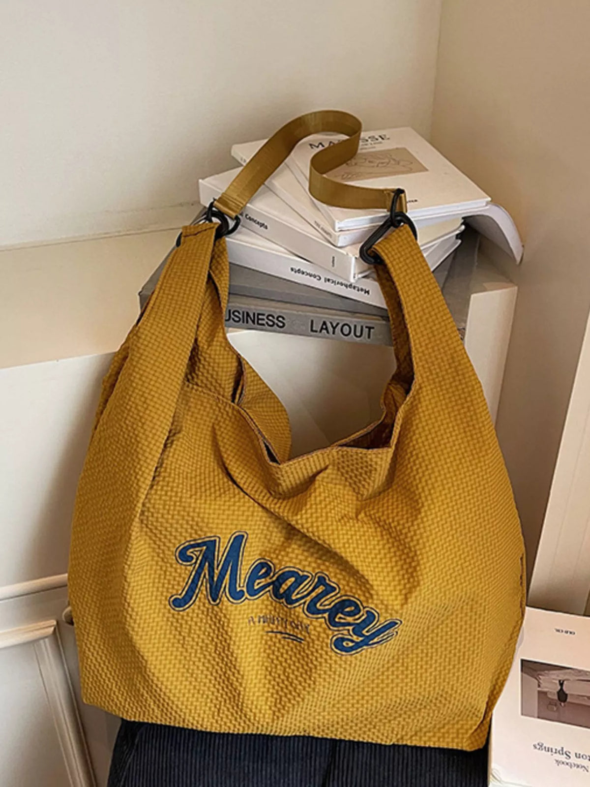 Yellow tote bag with 'Meaney' branding on a surface with books and papers.