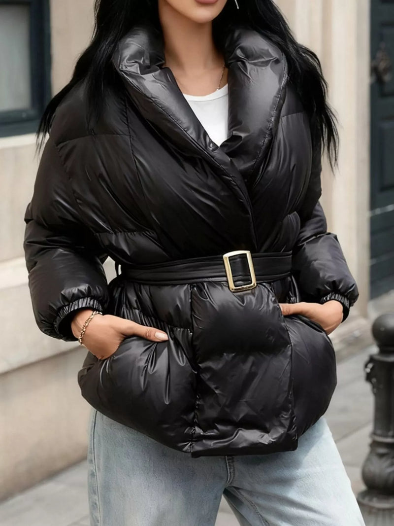 Person wearing a black puffer jacket with a belt, standing outdoors.