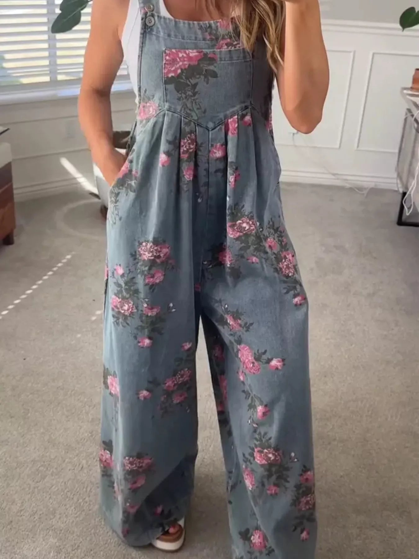 Person wearing a floral denim jumpsuit in a room with a window and rug.