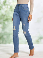 Person wearing blue distressed jeans against a blurred green background