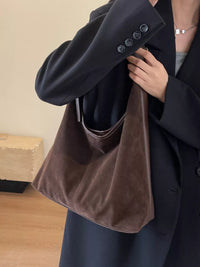 Person holding a brown towel in front of a dark coat against a beige wall.