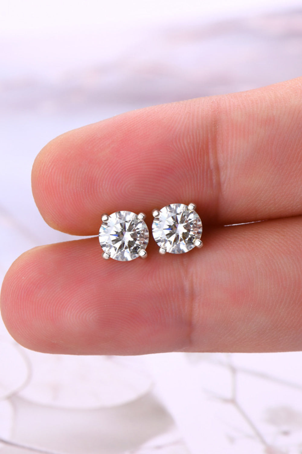 Pair of diamond stud earrings held between two fingers against a white background