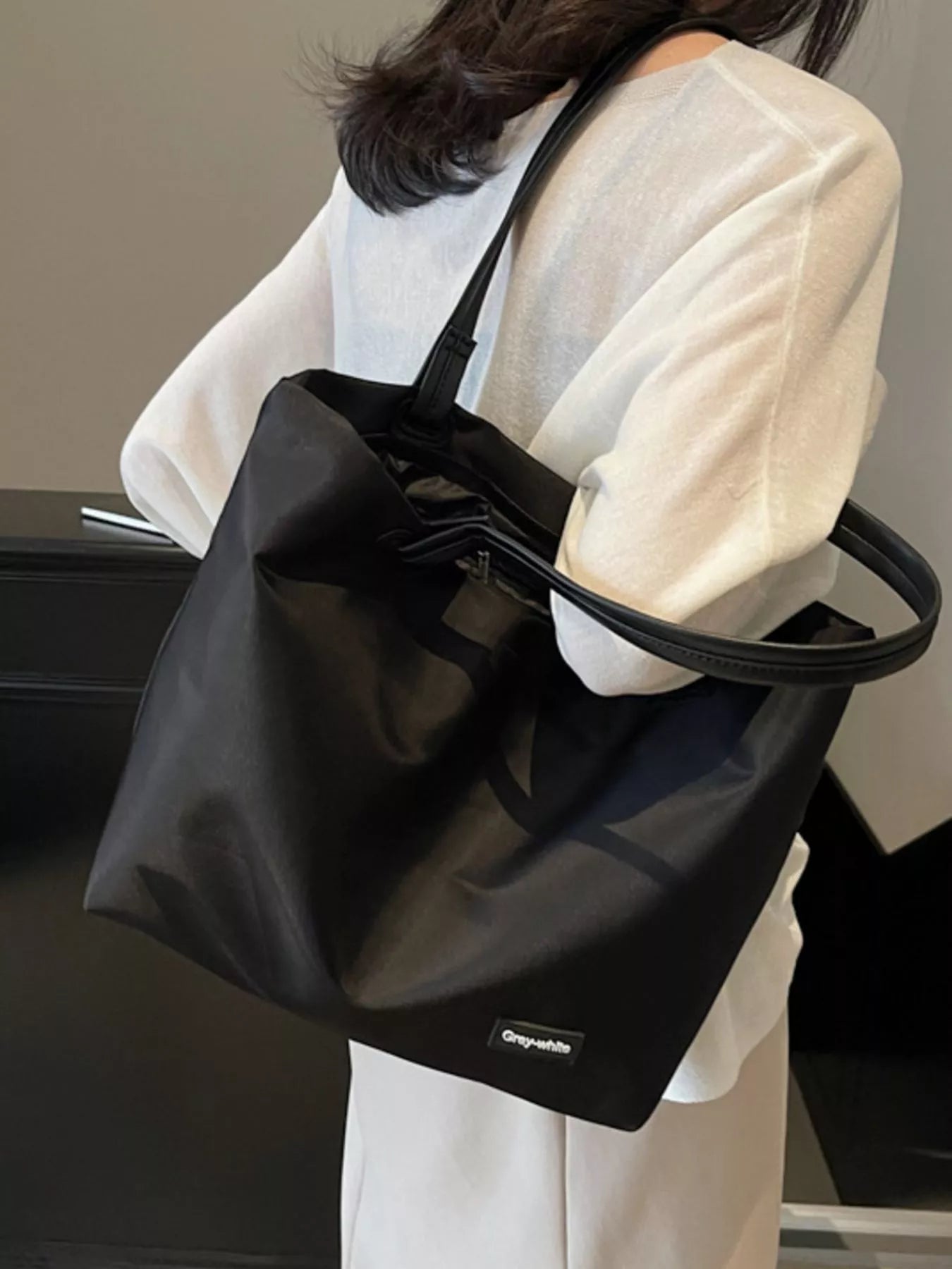 Person holding a black tote bag with a visible brand logo.