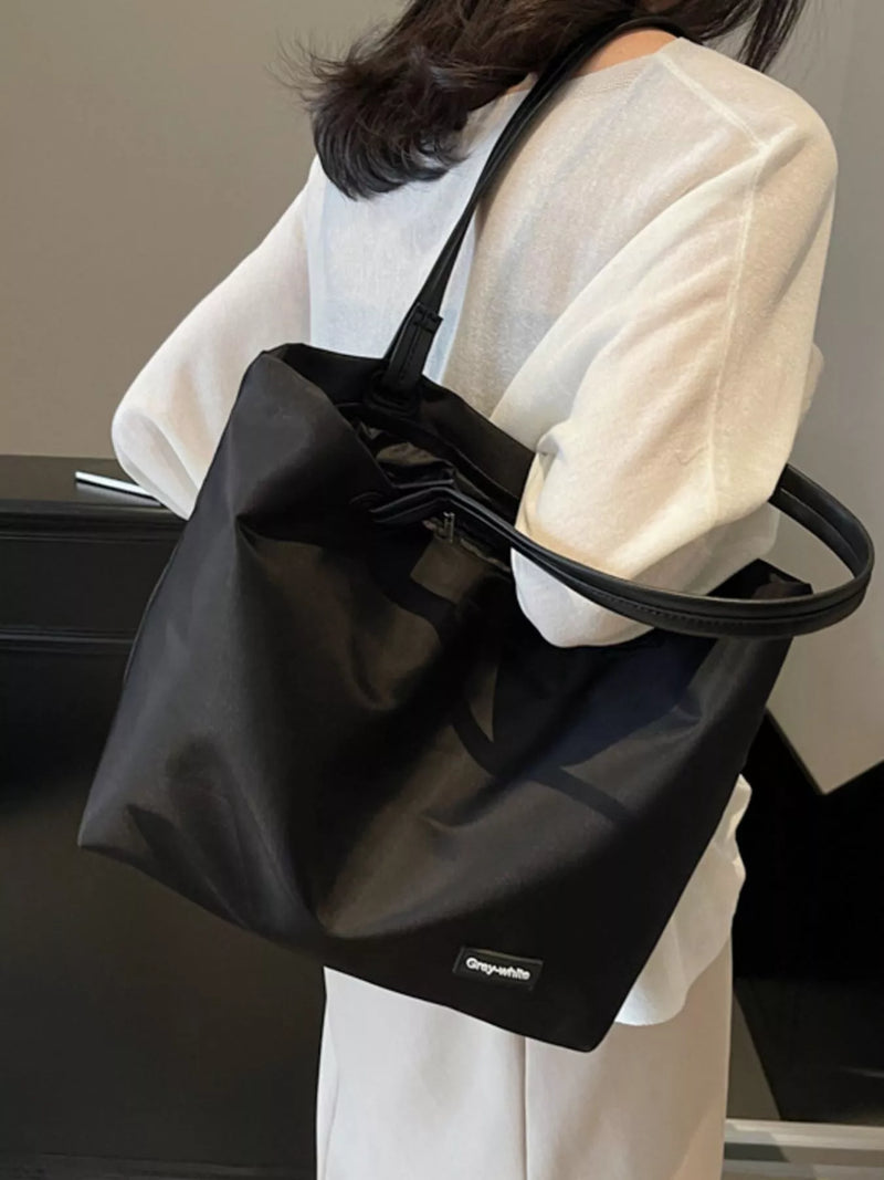 Person holding a black tote bag with a visible brand logo.
