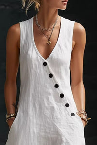White sleeveless dress with black buttons worn by a model against a dark background