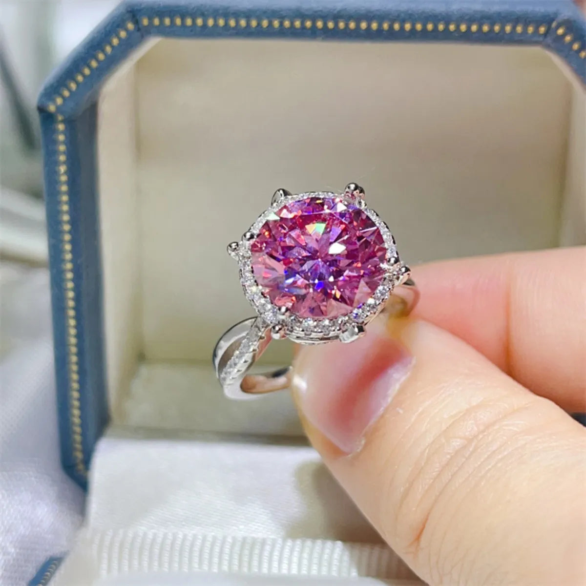 Pink gemstone ring held by a hand with a jewelry box in the background
