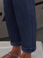 Close-up of a person's legs wearing dark blue denim pants with rolled cuffs and brown sandals.