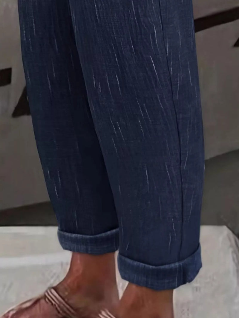 Close-up of a person's legs wearing dark blue denim pants with rolled cuffs and brown sandals.