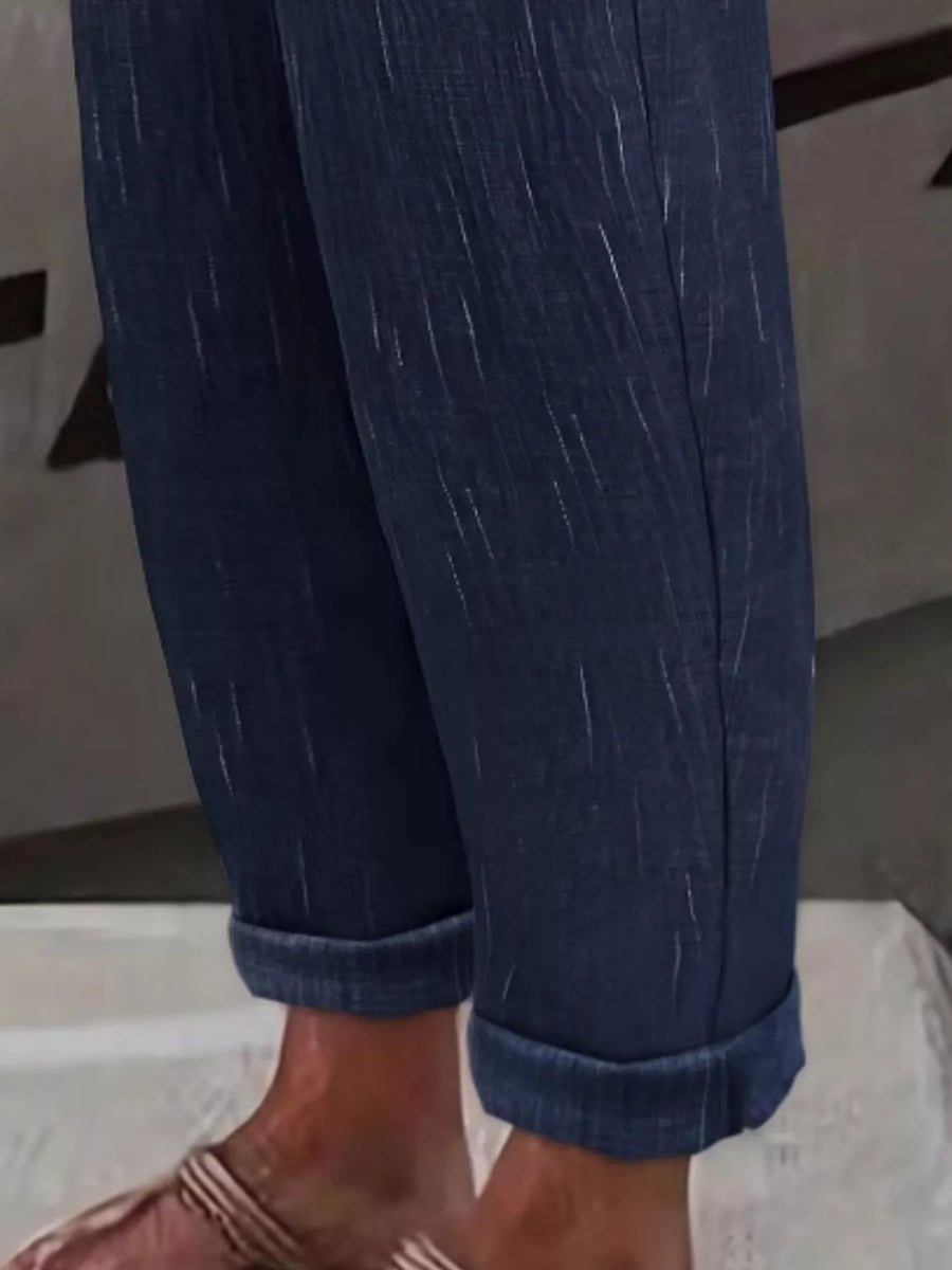 Close-up of a person's legs wearing dark blue denim pants with rolled cuffs and brown sandals.