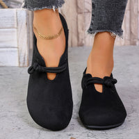 Black flat shoes with a knot detail worn by a person on a light background