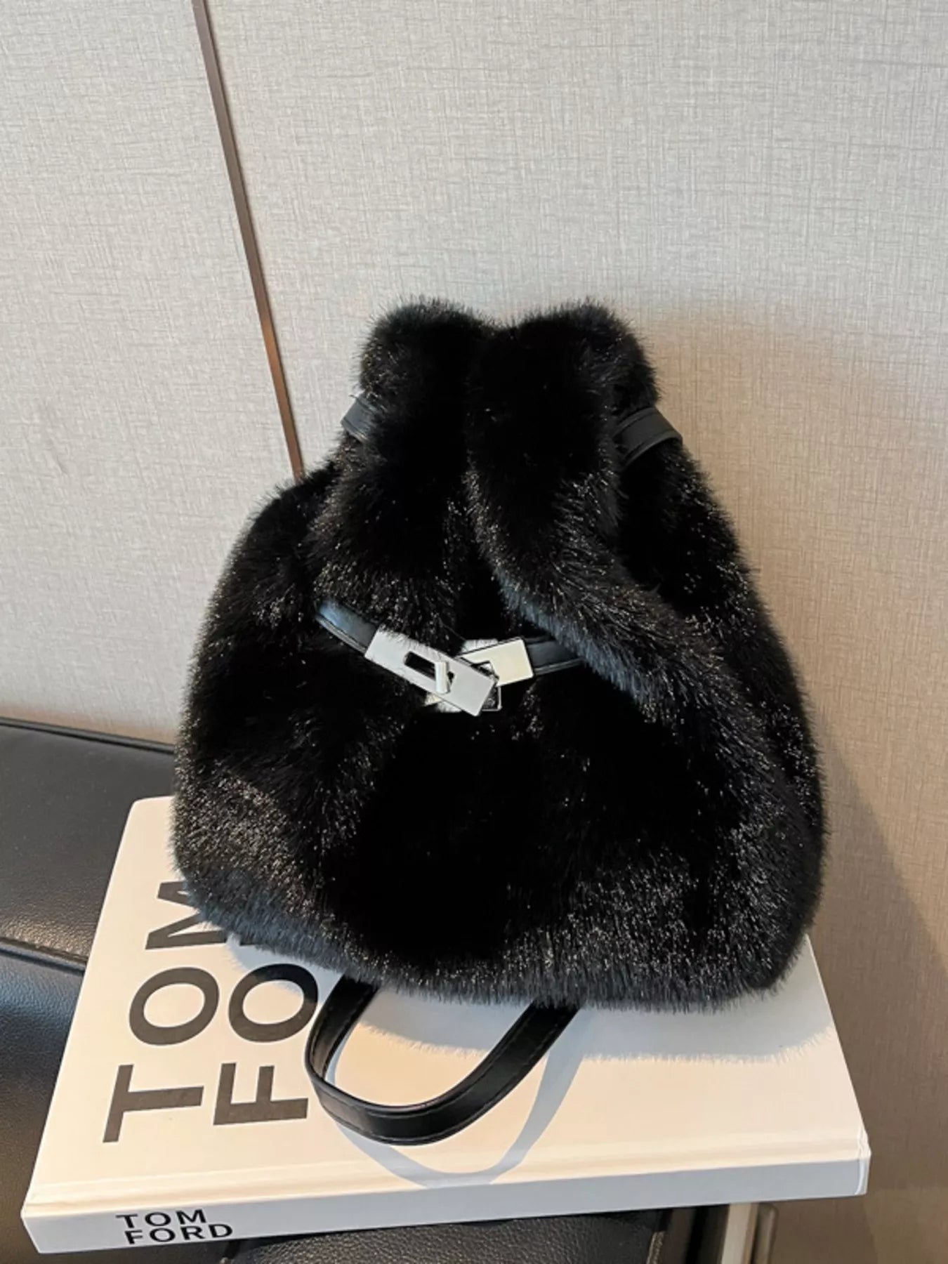 Black fluffy bag on a white surface with a blurred background