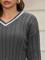 Gray cable knit sweater with a white V-neckline worn by a person.