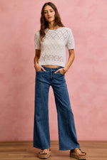 Woman wearing a white lace top and blue jeans against a pink background