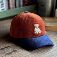 Red and blue cap with a teddy bear emblem on a wooden surface