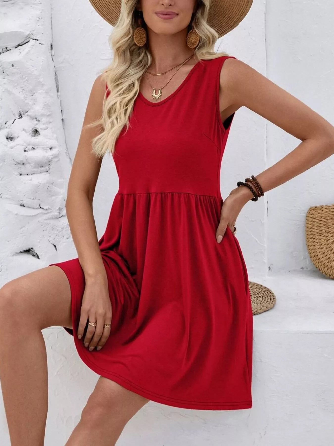 Woman wearing a red dress and straw hat against a white wall.