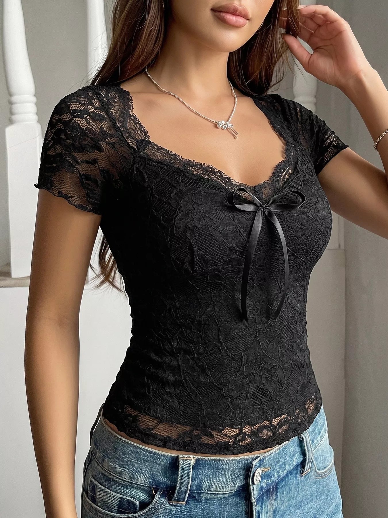 Black lace top with a bow detail worn by a person, against a neutral background