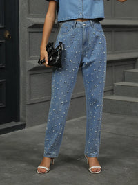 Person wearing blue jeans with pearl embellishments in an urban setting.
